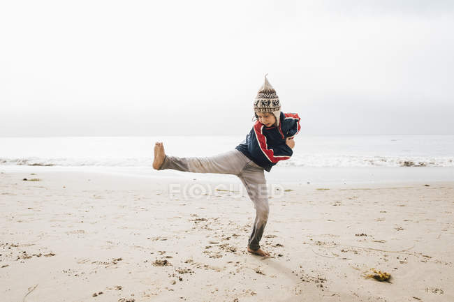 Мальчик балансирует на одной ноге на пляже — стоковое фото