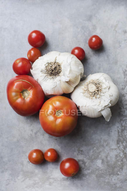 Vista superior de tomates frescos e alho na superfície cinzenta — Fotografia de Stock