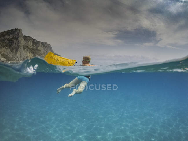 Sur la vue sous-marine du garçon regardant en arrière tout en nageant dans la mer bleue, Varigotti, Ligurie, Italie — Photo de stock