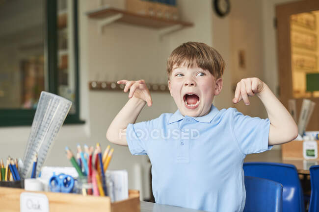 Primary schoolboy mimicking monster in classroom — Stock Photo