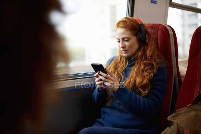 Женщина в поезде с мобильным телефоном и наушниками — стоковое фото