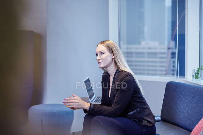 Donna d'affari sul divano in ufficio guardando altrove — Foto stock