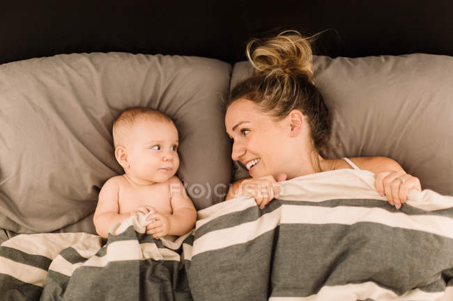 Mulher deitada na cama sob edredão com bebê filha — Fotografia de Stock