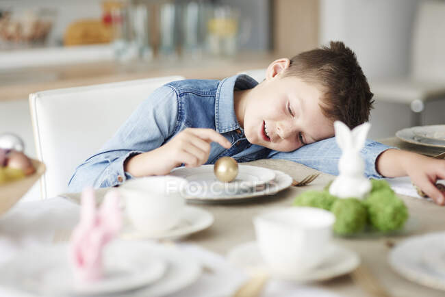 Хлопчик за обіднім столом грає з золотим пасхальним яйцем на тарілці — стокове фото