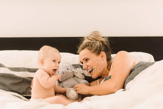 Mujer en la cama jugando con la hija bebé - foto de stock