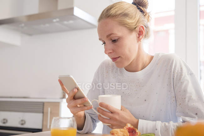 Giovane donna guardando smartphone a tavola colazione — Foto stock