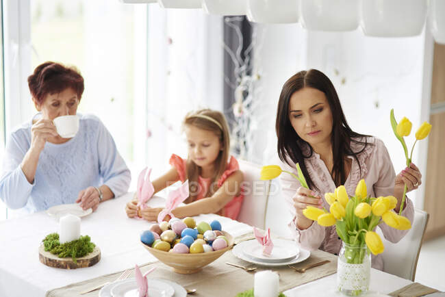 Mulher com filha e mãe organizando tulipas amarelas na mesa de jantar da Páscoa — Fotografia de Stock