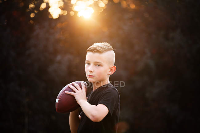 Retrato de menino segurando bola de futebol americano no jardim — Fotografia de Stock