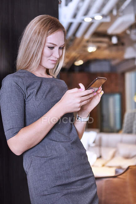Бізнес-леді в офісі, спираючись на стіну за допомогою смартфона — стокове фото