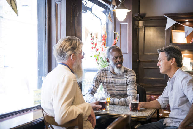 Trois hommes mûrs, assis ensemble dans un pub, parlant — Photo de stock
