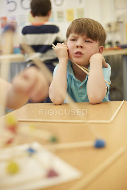 Primary schoolboy with plastic straws on classroom desks — Stock Photo