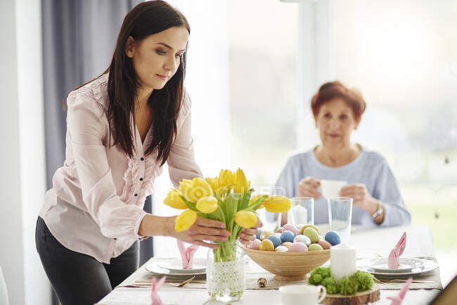 Mulher adulta média organizando tulipas amarelas na mesa de jantar da Páscoa — Fotografia de Stock