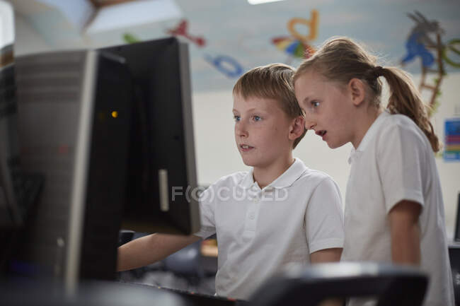 Школьник и девочка с помощью компьютера в классе в начальной школе — стоковое фото