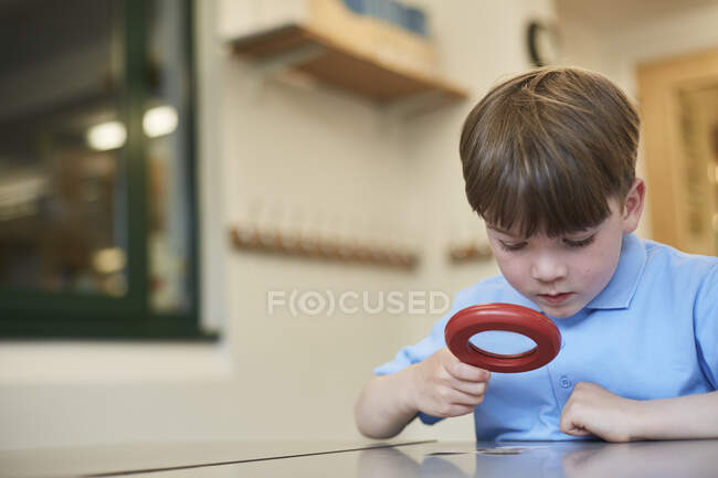 Schoolboy olhando através de lupa em sala de aula lição na escola primária — Fotografia de Stock