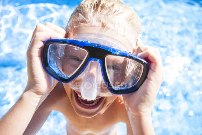 Portrait of boy wearing swimming goggles looking at camera smiling — Stock Photo
