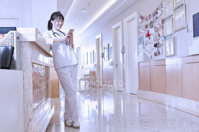 Doctor in hospital corridor using smartphone — Stock Photo