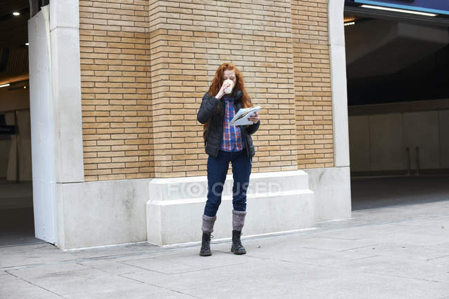 Mujer joven bebiendo café y sosteniendo el mapa en la calle - foto de stock