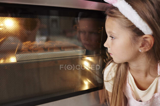 Girl watching easter biscuits in kitchen oven — Stock Photo