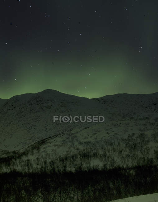 Aurora borealis sobre colinas cubiertas de nieve por la noche, Finnmark, Noruega - foto de stock
