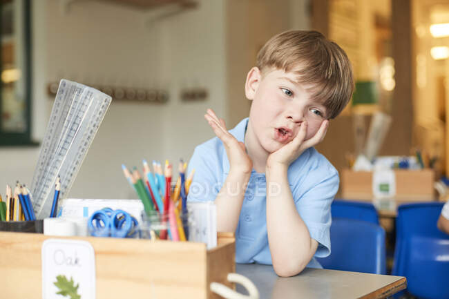 Aburrido colegial de primaria en el escritorio del aula - foto de stock