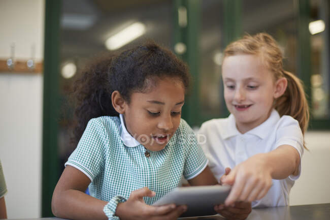 Дві школярки дивляться на цифровий планшет у класі в початковій школі — стокове фото
