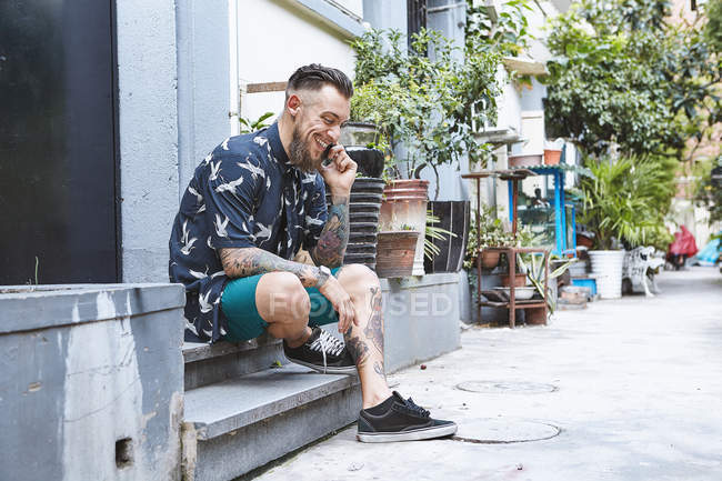 Молодий чоловік сидів на порозі в житлових провулку, роблячи смартфон виклику, Шанхай Французької концесії, Шанхай, Китай — стокове фото