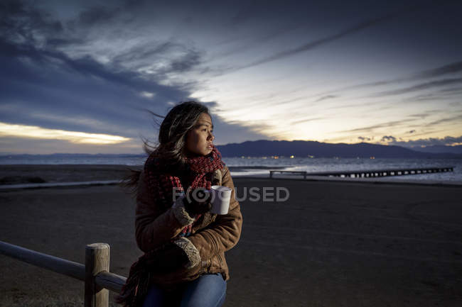 Young woman wrapped in scarf looking from beach at dusk — Stock Photo