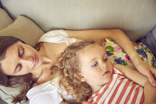 Mujer embarazada y su hija reclinada en el sofá - foto de stock