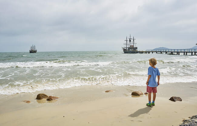 Мальчик на пляже, глядя вдаль на корабли в море, Панама, Санта-Катарина, Бразилия, Южная Америка — стоковое фото