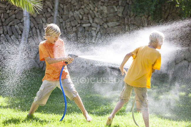 Jungen im Garten besprühen sich gegenseitig mit Wasser aus Schlauchleitung — Stockfoto