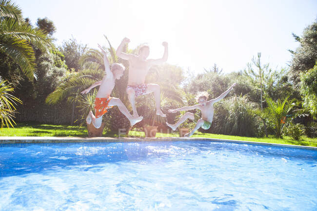 Father and sons in mid air jumping into outdoor swimming pool — Stock Photo