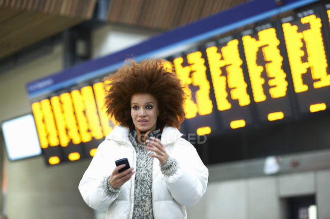 Молода жінка тримає смартфон на вокзалі — стокове фото