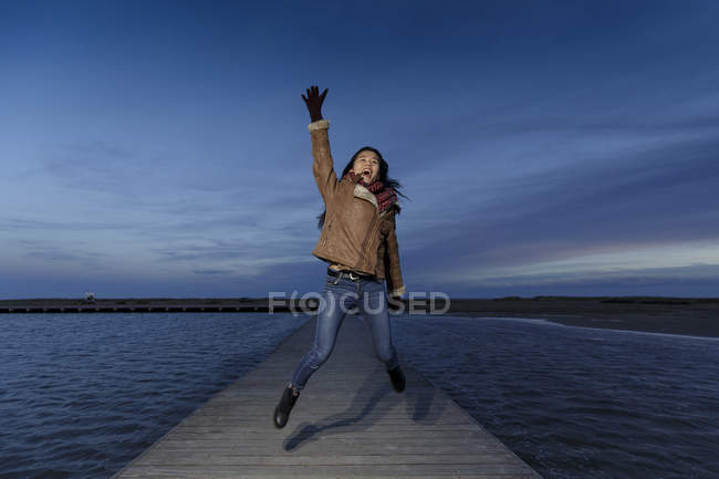 Young woman jumping on pier at dusk — Stock Photo