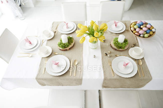 Прокладки для ушей кролика и миска с разноцветными пасхальными яйцами на обеденном столе — стоковое фото
