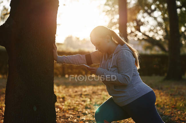 Curvaceous young woman training in park with smartphone — Stock Photo