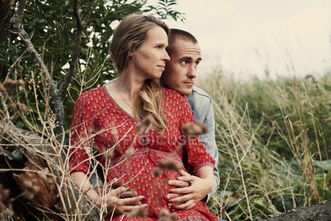 Романтическая беременная пара сидит на стволе дерева — стоковое фото