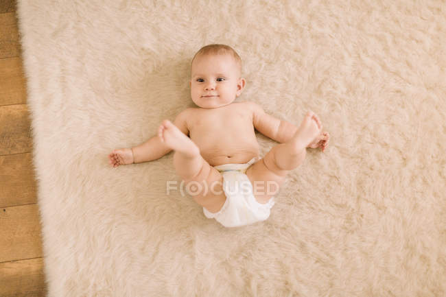 Portrait of cute baby girl in diaper lying on beige rug — Stock Photo