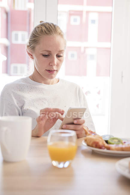 Молодая женщина, использующая смартфон за завтраком — стоковое фото