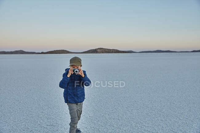 Молодий хлопчик стоїть на соляних квартирах, дивлячись крізь камеру, Салар де Уюні, Уюні, Оруро, Болівія, Південна Америка. — стокове фото