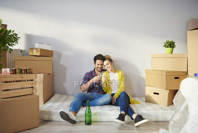 Молодая пара в окружении картонных коробок, пьющих шампанское — стоковое фото