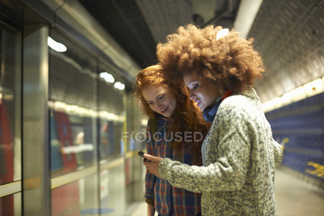 Two young women at train station looking at smartphone — Stock Photo