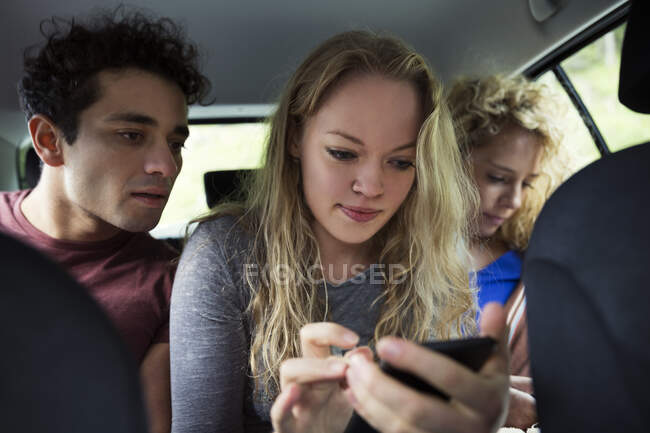 Друзья на заднем сиденье машины смотрят на смартфон — стоковое фото