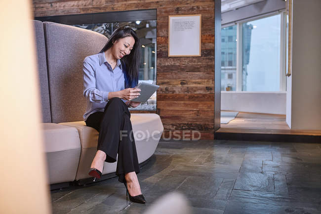 Femme d'affaires assise sur un canapé de bureau avec tablette numérique — Photo de stock