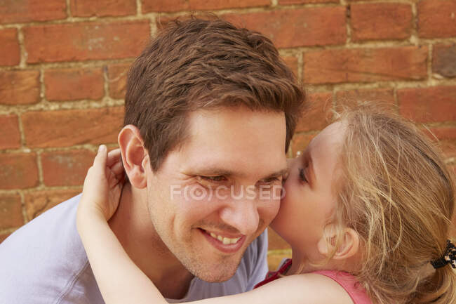 Девушка шепчет отцу на ухо кирпичной стеной, головой и плечом — стоковое фото