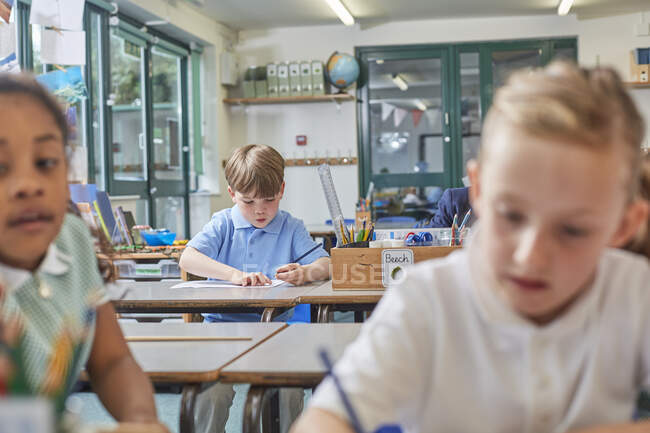 Estudante primário e meninas fazendo trabalhos escolares em mesas de sala de aula — Fotografia de Stock