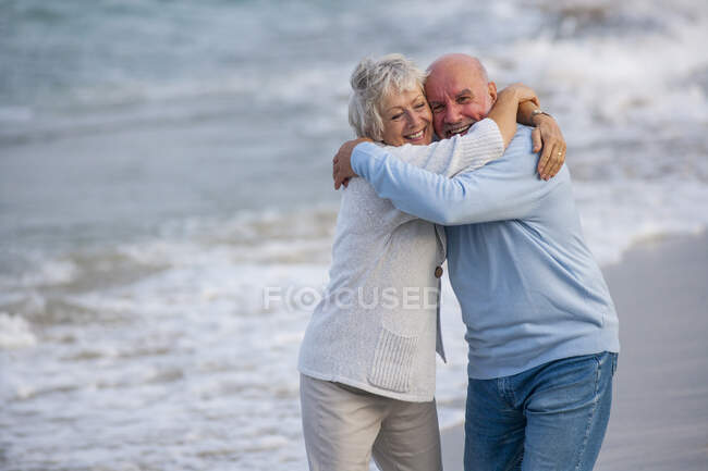 Pareja abrazándose y riendo a orillas del mar - foto de stock