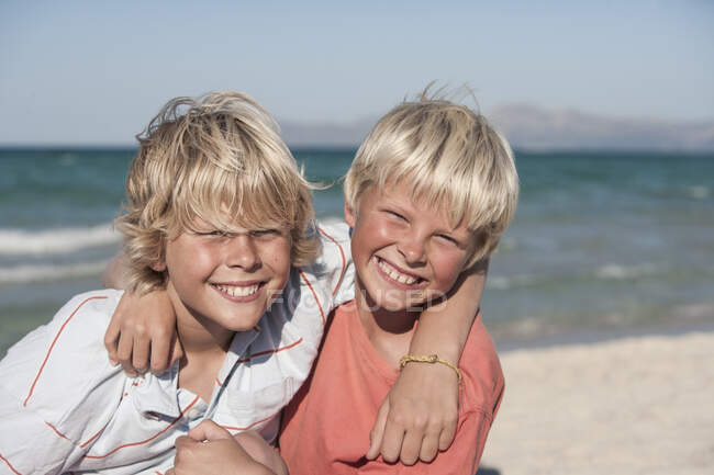 Retrato de hermanos sonrientes, brazos alrededor uno del otro, mirando a la cámara - foto de stock