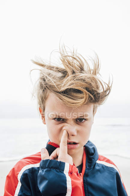 Portrait of boy on beach poking finger up nose — Stock Photo