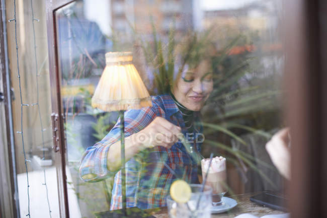 Vista através da janela da mulher no café apreciando chocolate quente — Fotografia de Stock