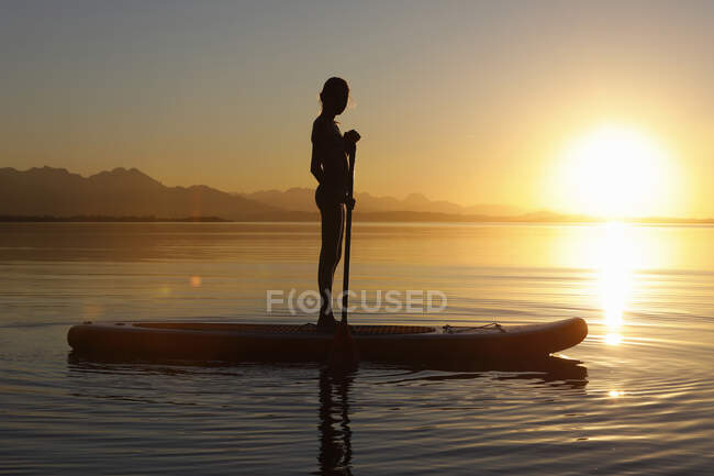 Giovane ragazza paddle imbarco sull'acqua, al tramonto — Foto stock